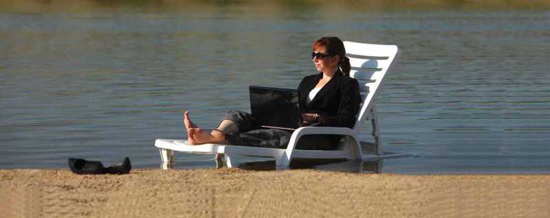 Woman on a lawn chair working on her laptop on a beach Woman on a lawn chair working on her laptop on a beach